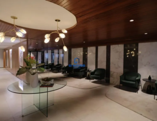 Piso: Material: Analisando a textura e o brilho, é provável que o piso seja feito de porcelanato polido de grande formato, imitando mármore. A ausência de porosidade visível sugere um acabamento impecável e fácil de limpar. Cor e Padrão: O bege suave com nuances creme apresenta variações sutis, imitando os padrões naturais do mármore. É possível observar veios delicados em tons mais claros, quebrando a monotonia e adicionando profundidade visual. Juntas: As juntas são tão finas que quase desaparecem, criando um efeito de continuidade e amplitude. O rejunte utilizado provavelmente é da mesma cor do piso, reforçando a uniformidade. Mesa Central: Tampo: O vidro temperado do tampo da mesa é cristalino e translúcido, permitindo que a luz o atravesse sem distorções. As bordas são polidas e arredondadas, garantindo segurança e um toque suave. Base: A base em forma de "X" é feita de vidro mais espesso, o que confere estabilidade e resistência à mesa. As peças de vidro são unidas por meio de encaixes precisos e discretos, sem parafusos ou colas visíveis. Detalhes: É possível que a mesa possua pequenos niveladores de altura nos pés, garantindo que ela fique perfeitamente estável, mesmo em pisos ligeiramente irregulares. Arranjo de Mesa: Vasos: Os vasos brancos são feitos de cerâmica de alta qualidade, com acabamento fosco ou acetinado. O design é minimalista, com linhas simples e elegantes. Plantas: As plantas parecem ser de espécies variadas, com diferentes tons de verde e texturas. Algumas podem ser folhagens tropicais, como filodendros ou zamioculcas, conhecidas por sua resistência e beleza. Livro: O livro aberto sobre a mesa tem uma capa escura, possivelmente em couro ou tecido aveludado. As páginas internas parecem ser de papel de alta gramatura, com impressão de qualidade. Composição: A disposição dos vasos, plantas e livro é cuidadosamente pensada para criar um ponto focal interessante e equilibrado. A altura dos elementos varia, criando uma dinâmica visual agradável. Iluminação: Rebaixo: O rebaixo no teto possui bordas arredondadas e um acabamento impecável. A iluminação embutida é feita com lâmpadas LED de alta eficiência, que proporcionam uma luz brilhante e uniforme. Pendentes: Os pendentes dourados são feitos de metal com acabamento escovado ou polido. Os "galhos" são delicados e sinuosos, com detalhes que imitam a forma de ramos de árvores. Luminárias: As luminárias em forma de pétalas são feitas de vidro fosco ou acrílico, que difunde a luz de forma suave e uniforme. A cor da luz é quente e aconchegante, criando uma atmosfera relaxante. Paredes: Mármore: O mármore branco com veios cinzas é de alta qualidade, com um acabamento polido que realça sua beleza natural. Os veios cinzas são únicos em cada placa, tornando o revestimento exclusivo. Madeira: Os painéis de madeira escura são feitos de madeira nobre, como nogueira ou ébano. O acabamento é impecável, com verniz de alta resistência que protege a madeira e realça sua beleza. Detalhes: A junção entre os painéis de mármore e madeira é perfeita, sem folgas ou irregularidades. A altura dos painéis é cuidadosamente calculada para criar uma proporção visualmente agradável. Mobiliário: Poltronas: As poltronas de veludo verde escuro possuem uma estrutura interna resistente, feita de madeira maciça ou metal. O estofamento é macio e confortável, com enchimento de espuma de alta densidade. Mesas Laterais: As mesas laterais redondas são feitas de metal com acabamento escuro, como preto fosco ou bronze. O design é minimalista, com linhas simples e elegantes. Detalhes: As poltronas possuem pés discretos, que elevam o assento do chão e facilitam a limpeza. As mesas laterais são leves e fáceis de mover, permitindo que sejam reposicionadas conforme necessário. Detalhes Finais: Acústica: O ambiente possui boa acústica, com materiais que absorvem o som e reduzem o eco. Isso contribui para criar uma atmosfera tranquila e relaxante. Climatização: O sistema de climatização é eficiente e silencioso, mantendo a temperatura agradável em todas as estações do ano. Acessibilidade: O ambiente é acessível a pessoas com mobilidade reduzida, com rampas de acesso e espaços amplos para circulação. Cada detalhe, por menor que seja, contribui para criar um ambiente de recepção que transmite elegância, sofisticação e conforto. A atenção aos detalhes é evidente em cada escolha de material, cor, iluminação e mobiliário, resultando em um espaço harmonioso e convidativo.