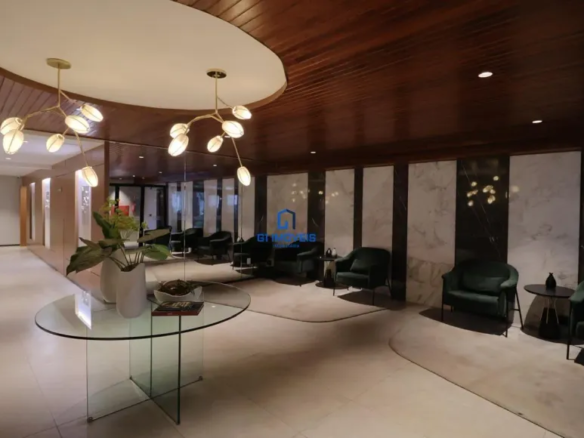 Piso: Material: Analisando a textura e o brilho, é provável que o piso seja feito de porcelanato polido de grande formato, imitando mármore. A ausência de porosidade visível sugere um acabamento impecável e fácil de limpar. Cor e Padrão: O bege suave com nuances creme apresenta variações sutis, imitando os padrões naturais do mármore. É possível observar veios delicados em tons mais claros, quebrando a monotonia e adicionando profundidade visual. Juntas: As juntas são tão finas que quase desaparecem, criando um efeito de continuidade e amplitude. O rejunte utilizado provavelmente é da mesma cor do piso, reforçando a uniformidade. Mesa Central: Tampo: O vidro temperado do tampo da mesa é cristalino e translúcido, permitindo que a luz o atravesse sem distorções. As bordas são polidas e arredondadas, garantindo segurança e um toque suave. Base: A base em forma de "X" é feita de vidro mais espesso, o que confere estabilidade e resistência à mesa. As peças de vidro são unidas por meio de encaixes precisos e discretos, sem parafusos ou colas visíveis. Detalhes: É possível que a mesa possua pequenos niveladores de altura nos pés, garantindo que ela fique perfeitamente estável, mesmo em pisos ligeiramente irregulares. Arranjo de Mesa: Vasos: Os vasos brancos são feitos de cerâmica de alta qualidade, com acabamento fosco ou acetinado. O design é minimalista, com linhas simples e elegantes. Plantas: As plantas parecem ser de espécies variadas, com diferentes tons de verde e texturas. Algumas podem ser folhagens tropicais, como filodendros ou zamioculcas, conhecidas por sua resistência e beleza. Livro: O livro aberto sobre a mesa tem uma capa escura, possivelmente em couro ou tecido aveludado. As páginas internas parecem ser de papel de alta gramatura, com impressão de qualidade. Composição: A disposição dos vasos, plantas e livro é cuidadosamente pensada para criar um ponto focal interessante e equilibrado. A altura dos elementos varia, criando uma dinâmica visual agradável. Iluminação: Rebaixo: O rebaixo no teto possui bordas arredondadas e um acabamento impecável. A iluminação embutida é feita com lâmpadas LED de alta eficiência, que proporcionam uma luz brilhante e uniforme. Pendentes: Os pendentes dourados são feitos de metal com acabamento escovado ou polido. Os "galhos" são delicados e sinuosos, com detalhes que imitam a forma de ramos de árvores. Luminárias: As luminárias em forma de pétalas são feitas de vidro fosco ou acrílico, que difunde a luz de forma suave e uniforme. A cor da luz é quente e aconchegante, criando uma atmosfera relaxante. Paredes: Mármore: O mármore branco com veios cinzas é de alta qualidade, com um acabamento polido que realça sua beleza natural. Os veios cinzas são únicos em cada placa, tornando o revestimento exclusivo. Madeira: Os painéis de madeira escura são feitos de madeira nobre, como nogueira ou ébano. O acabamento é impecável, com verniz de alta resistência que protege a madeira e realça sua beleza. Detalhes: A junção entre os painéis de mármore e madeira é perfeita, sem folgas ou irregularidades. A altura dos painéis é cuidadosamente calculada para criar uma proporção visualmente agradável. Mobiliário: Poltronas: As poltronas de veludo verde escuro possuem uma estrutura interna resistente, feita de madeira maciça ou metal. O estofamento é macio e confortável, com enchimento de espuma de alta densidade. Mesas Laterais: As mesas laterais redondas são feitas de metal com acabamento escuro, como preto fosco ou bronze. O design é minimalista, com linhas simples e elegantes. Detalhes: As poltronas possuem pés discretos, que elevam o assento do chão e facilitam a limpeza. As mesas laterais são leves e fáceis de mover, permitindo que sejam reposicionadas conforme necessário. Detalhes Finais: Acústica: O ambiente possui boa acústica, com materiais que absorvem o som e reduzem o eco. Isso contribui para criar uma atmosfera tranquila e relaxante. Climatização: O sistema de climatização é eficiente e silencioso, mantendo a temperatura agradável em todas as estações do ano. Acessibilidade: O ambiente é acessível a pessoas com mobilidade reduzida, com rampas de acesso e espaços amplos para circulação. Cada detalhe, por menor que seja, contribui para criar um ambiente de recepção que transmite elegância, sofisticação e conforto. A atenção aos detalhes é evidente em cada escolha de material, cor, iluminação e mobiliário, resultando em um espaço harmonioso e convidativo.
