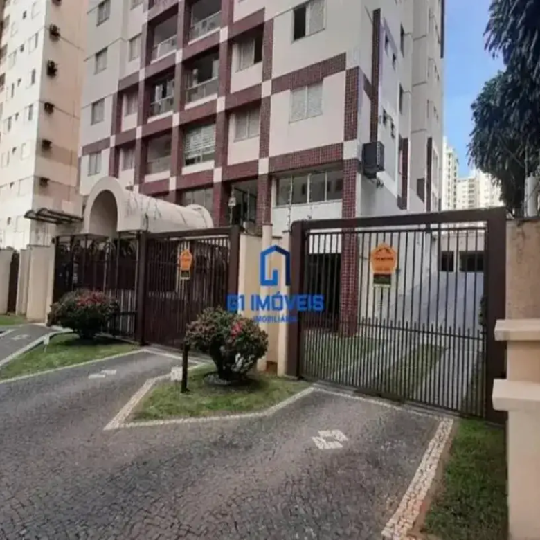 A imagem é a fachada do residencial canoeiros no setor bueno uma área urbana, com um foco na entrada principal e nos detalhes de segurança. A cena é iluminada pela luz do dia, e a composição equilibra elementos arquitetônicos com áreas verdes. Edifício: Altura e Estrutura: O prédio é alto, composto por múltiplos andares. A arquitetura sugere um design moderno, mas com alguns elementos decorativos mais tradicionais. Fachada: A fachada combina painéis em tons claros, possivelmente bege ou branco, com detalhes quadriculados em tons de tijolo ou marrom avermelhado. Esses detalhes criam um padrão visual interessante, quebrando a monotonia da fachada. Janelas: As janelas são padronizadas, retangulares e dispostas de forma simétrica em cada andar. Elas parecem ser de vidro claro com molduras claras ou metálicas. Entrada: A entrada principal do prédio é emoldurada por uma estrutura arqueada, que se projeta para a frente. Essa área é sombreada e pode ter detalhes adicionais, como luminárias. Ar Condicionado: Em uma das laterais do prédio, é possível observar aparelhos de ar condicionado instalados nas janelas, indicando que o sistema de climatização é individual. Portão e Entrada: Material e Design: O portão é feito de metal, possivelmente ferro forjado, e tem um design com barras verticais e detalhes ornamentais. A cor é um tom escuro, como marrom ou preto, que contrasta com a vegetação ao redor. Segurança: Há avisos de segurança fixados no portão, indicando a presença de vigilância ou de um sistema de segurança ativo. Paisagismo: A área ao redor do portão é bem cuidada, com grama aparada e arbustos decorativos. Há um caminho de pedra que leva do portão até a entrada do prédio. Iluminação: Uma pequena luminária está presente em meio à vegetação próxima ao portão, sugerindo iluminação noturna para a área. Segurança Adicional: Muro e Arame Farpado: À direita da imagem, há um muro que delimita a propriedade. No topo do muro, há arame farpado, indicando uma preocupação adicional com a segurança do local. Sistema de Alarme: Também visível na parede, encontra-se um sistema de alarme com luzes de advertência, reforçando a segurança do prédio. Ambiente: Vegetação: A presença de árvores e arbustos ao redor do prédio sugere que ele está localizado em uma área com alguma vegetação, possivelmente um bairro residencial com áreas verdes. Pavimentação: O chão é pavimentado com pedras, criando um padrão interessante e funcional para o trânsito de veículos e pedestres. Céu: O céu azul claro indica um dia ensolarado, contribuindo para uma atmosfera geral positiva na imagem. Logotipo: G1 Imóveis: No centro da imagem, sobre o portão, há um logotipo da imobiliária "G1 Imóveis". Em resumo, a imagem detalha um edifício de apartamentos com uma fachada bem cuidada, um portão de entrada com segurança reforçada e um paisagismo que valoriza a área. A combinação de elementos arquitetônicos e naturais cria uma atmosfera convidativa e segura.