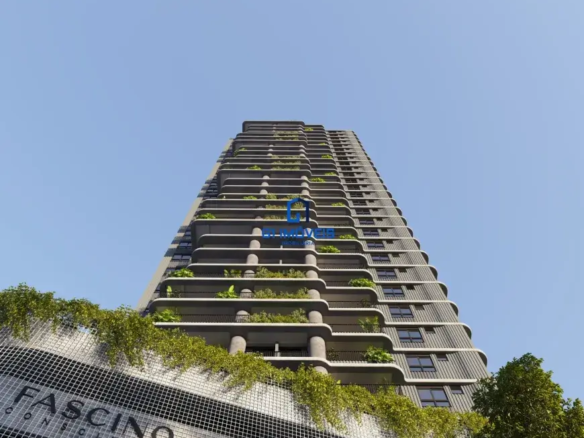 Edifício: Estrutura: A estrutura principal é um arranha-céu moderno. O concreto cinza parece ter um acabamento ligeiramente texturizado, possivelmente com padrões lineares ou sulcos sutis que correm verticalmente, adicionando uma dimensão visual ao material. Varandas: As varandas são o ponto focal do design. Elas se projetam horizontalmente em cada andar, criando uma série de níveis escalonados. As bordas das varandas têm um contorno suavemente arredondado, conferindo um toque orgânico ao design. Vegetação: A vegetação nas varandas é diversificada. Há plantas de folhagem densa e de cor verde escura, algumas parecendo ser arbustos pequenos e outras, plantas rastejantes que caem em cascata pelas bordas das varandas. A vegetação não é uniforme, com algumas áreas mais densas que outras, criando um padrão natural e irregular. Colunas: As colunas de concreto que suportam as varandas são cilíndricas e parecem ter um acabamento liso. Elas estão posicionadas de forma estratégica para suportar o peso das varandas e das plantas. Janelas: As janelas são pequenas e retangulares, com molduras escuras. Sua distribuição uniforme cria um padrão repetitivo que complementa a horizontalidade das varandas. Base do Edifício: Fachada: A fachada da base do edifício é feita de uma tela quadriculada, possivelmente de metal ou outro material resistente. Essa tela serve como suporte para plantas trepadeiras, criando um muro verde vertical. Inscrição "FASCINO": As letras da inscrição "FASCINO" são grandes e parecem ser feitas de um material metálico com acabamento fosco. As letras são sombreadas, dando uma sensação de profundidade e dimensão. A fonte é moderna e elegante, alinhada com o design geral do edifício. Vegetação Pendurada: A vegetação que pende da tela quadriculada é exuberante e variada, com diferentes tons de verde e texturas. Algumas plantas têm folhas pequenas e delicadas, enquanto outras têm folhas maiores e mais arredondadas. Ambiente: Céu: O céu azul claro é uniforme e sem nuvens, proporcionando um fundo limpo e vibrante para o edifício. Luz: A luz do sol incide sobre o edifício de um ângulo ligeiramente lateral, criando sombras sutis que realçam a textura dos materiais e a profundidade da vegetação. Vegetação Adjacente: No lado direito da imagem, há uma árvore com folhagem densa, que adiciona uma dimensão adicional de verde ao ambiente. Cores: Predominantes: As cores predominantes são o cinza do concreto, o verde da vegetação e o azul do céu. Complementares: Há toques de cores mais escuras nas janelas e na inscrição "FASCINO", que contrastam com o cinza claro do concreto. Variações: A vegetação apresenta uma variedade de tons de verde, desde o verde claro até o verde escuro, criando um efeito visual interessante e natural. Em resumo, a imagem retrata um edifício moderno e sofisticado, com um design inovador que integra elementos naturais à arquitetura urbana. Os detalhes dos materiais, a vegetação exuberante e a luz do sol criam uma composição visualmente atraente e convidativa.