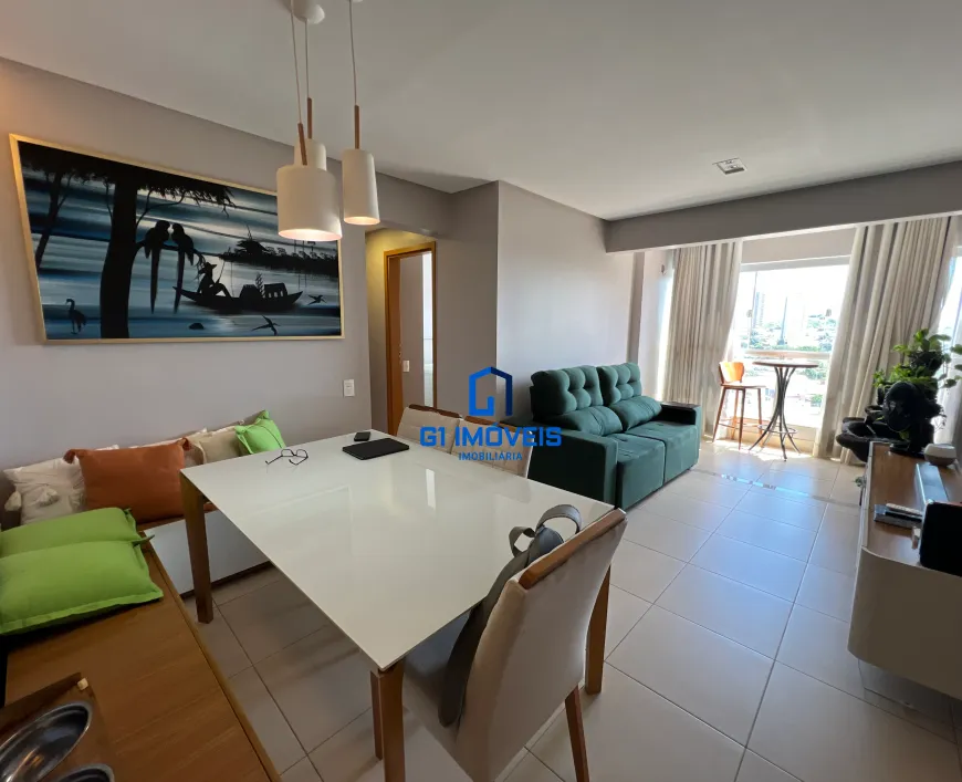 Paredes e Estrutura: Cor das Paredes: As paredes são de um cinza bem claro, quase um bege acinzentado. A cor é fosca, o que ajuda a absorver a luz e suavizar o ambiente. Nota-se um rodapé branco discreto que acompanha todo o perímetro, criando uma transição suave entre a parede e o piso. Teto: O teto é branco e aparentemente liso, com um acabamento que reflete bem a luz. Há um discreto detalhe de moldura no encontro do teto com a parede. Área de Jantar: Mesa: A mesa tem um tampo de vidro ou material similar, com um brilho que reflete a luz das luminárias acima. A base da mesa é de madeira clara, com um design simples e elegante. Cadeiras: As cadeiras possuem um design clássico com pernas de madeira clara e assentos estofados em um tecido bege claro, com textura sutil. O encosto das cadeiras tem uma curvatura que sugere conforto. Banco/Sofá Lateral: O banco que acompanha a mesa é embutido e possui um acabamento em madeira de tonalidade mel. As almofadas dispostas sobre o banco são de diferentes cores e tamanhos: duas almofadas quadradas grandes em verde-limão vibrante, uma almofada retangular em tom laranja-terracota e outra almofada em tom creme claro com uma leve textura. Luminárias: As luminárias pendentes são cilíndricas e brancas, com detalhes em madeira clara que combinam com a mesa e as cadeiras. Cada luminária possui um cabo fino que a suspende do teto. Quadro: O quadro na parede é grande e emoldurado com uma moldura dourada fina. A pintura retrata uma cena ribeirinha com árvores escuras em silhueta, um rio com reflexos de luz e uma canoa com uma figura humana. Há também aves representadas na pintura, adicionando um toque de vida à cena. Detalhes: Um interruptor e uma tomada brancos discretos estão visíveis na parede, próximos à mesa. Sala de Estar: Sofá: O sofá é de um verde esmeralda intenso. É um sofá modular, composto por dois blocos que se encaixam. O estofamento parece ser de veludo ou um tecido similar, com um toque aveludado. O sofá tem um design moderno, com linhas retas e almofadas soltas no encosto. Mesa Lateral: Uma pequena mesa redonda de madeira com duas cadeiras de vime é colocada perto da janela. Cortinas: As cortinas são de um tecido leve e translúcido, permitindo a passagem de luz natural, mas oferecendo privacidade. Elas são de cor branca ou creme claro. Móvel de TV: Próximo à janela há um móvel de TV em tons neutros, com um design minimalista e moderno. Sobre o móvel, há uma televisão de tela plana e um objeto decorativo. Plantas: Ao lado da TV, há uma planta em um vaso. Outros Detalhes: Piso: O piso é revestido por cerâmica ou porcelanato em um tom bege claro. As peças são grandes e quadradas, com juntas discretas. Porta: Ao lado da área de jantar, há uma porta de madeira clara que leva a outro cômodo do apartamento. Iluminação: A iluminação geral do apartamento é boa, com bastante luz natural entrando pelas janelas e luz artificial proveniente das luminárias. Em resumo, o apartamento é um espaço bem planejado e decorado, com atenção aos detalhes e uma paleta de cores que transmite conforto e elegância. A combinação de elementos modernos e clássicos cria um ambiente acolhedor e convidativo.