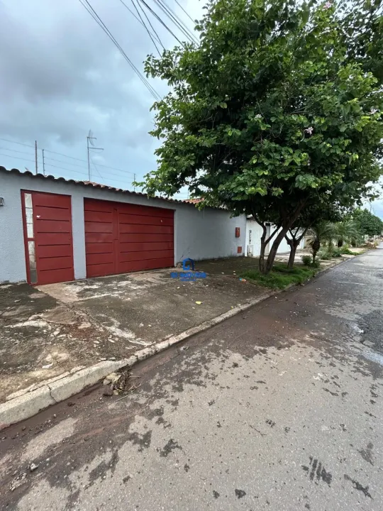 538533134313914 A imagem mostra uma casa térrea com um design simples e funcional. A fachada é pintada em um tom de cinza claro, que contrasta com as portas da garagem, pintadas em um tom vibrante de vermelho. A casa possui um telhado com ondas e é construída em um estilo minimalista, sem muitos detalhes ornamentais. Em frente à casa, há uma área de concreto que serve como entrada e garagem. Esta área parece estar um pouco suja e desgastada, com manchas e pequenas rachaduras. Há também um pequeno jardim com grama e algumas plantas, incluindo uma árvore grande e frondosa que oferece sombra à casa. A rua em frente à casa é asfaltada e apresenta sinais de umidade, sugerindo que pode ter chovido recentemente. No geral, a imagem transmite uma sensação de simplicidade e praticidade, com um toque de cor nas portas da garagem.