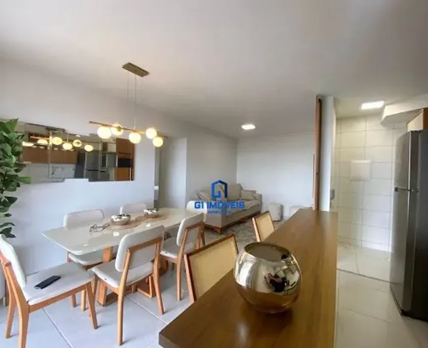 Primeiro Plano: Bancada: A madeira da bancada não é apenas de um tom médio, mas parece ter um acabamento liso e ligeiramente brilhante, sugerindo um verniz ou selante que realça os veios da madeira. É possível que seja uma madeira nobre como ipê ou jatobá, dada a sua tonalidade e aparente densidade. Vaso: O vaso dourado, além de esférico, tem um brilho intenso que reflete a luz do ambiente, criando pequenos pontos de luz que se espalham ao redor. A superfície do vaso pode ter um leve padrão texturizado, quase imperceptível à distância, mas que adiciona profundidade ao objeto. Profundidade: É possível notar uma leve profundidade de campo, que da destaque a bancada em primeiro plano. Mesa de Jantar: Tampo da Mesa: O tampo da mesa, ao ser examinado mais de perto, revela sutis veios ou padrões que sugerem ser mármore carrara ou um material sintético de alta qualidade que imita a aparência do mármore. As bordas da mesa são levemente arredondadas, o que confere um toque de suavidade ao design. Cadeiras: As cadeiras têm uma estrutura de madeira clara com um design minimalista e elegante. Os assentos e encostos estofados parecem ser feitos de um tecido texturizado, possivelmente linho ou algodão, com uma cor que varia entre o branco e o bege claro, criando um contraste suave com a madeira. Os detalhes de costura nos estofados são discretos, mas refinados. Objetos Decorativos: Os pequenos objetos sobre a mesa incluem um centro de mesa com elementos decorativos como vasos pequenos ou porta guardanapos, adicionando um toque de personalidade ao espaço. Um controle remoto, deixado sobre uma das cadeiras, sugere que o ambiente é utilizado com frequência e de forma prática. Iluminação: Luminária: A luminária pendente é composta por uma barra horizontal de metal dourado ou latão, da qual pendem várias esferas de vidro opalino que emitem uma luz suave e difusa. A disposição das esferas é irregular, o que confere um toque moderno e artístico à peça. A luz emitida pela luminária cria um ambiente acolhedor e convidativo. Reflexo no Espelho: Cozinha: O reflexo no espelho revela detalhes adicionais da cozinha, como armários com puxadores discretos e uma bancada de granito ou quartzo. A geladeira de aço inoxidável tem um acabamento escovado que evita marcas de dedos e confere um aspecto limpo e moderno. A iluminação na cozinha é complementada por spots embutidos no teto, que garantem uma iluminação uniforme e funcional. Ambiente Geral: Paredes e Piso: A cor clara das paredes e do piso amplia a sensação de espaço e luminosidade, criando um ambiente leve e arejado. As paredes têm um acabamento liso e uniforme, enquanto o piso de cerâmica tem juntas discretas que não comprometem a estética geral do ambiente. Planta: A planta no canto esquerdo adiciona um toque de frescor e vitalidade ao espaço. As folhas da planta são de um verde intenso e brilhante, e o vaso em que está plantada complementa a decoração do ambiente. Sala de Estar: Ao fundo, na área da sala de estar, o sofá claro parece ser revestido em um tecido macio e confortável, como veludo ou chenille. O puff complementa o sofá e oferece um espaço adicional para relaxar. Almofadas decorativas em tons neutros ou pastel adicionam um toque de cor e textura ao ambiente. Detalhes Adicionais: Rodapés: Os rodapés são discretos e acompanham a cor das paredes, criando uma transição suave entre as paredes e o piso. Portas e Janelas: As portas e janelas são emolduradas em madeira clara ou branca, o que harmoniza com o restante da decoração. As janelas são amplas e permitem a entrada de luz natural, o que contribui para a sensação de amplitude e luminosidade do ambiente. Em resumo, a imagem retrata um imóvel com um design moderno e elegante, onde cada detalhe foi cuidadosamente pensado para criar um ambiente acolhedor, funcional e esteticamente agradável. A combinação de cores claras, materiais nobres e elementos decorativos refinados confere ao espaço um toque de sofisticação e conforto.