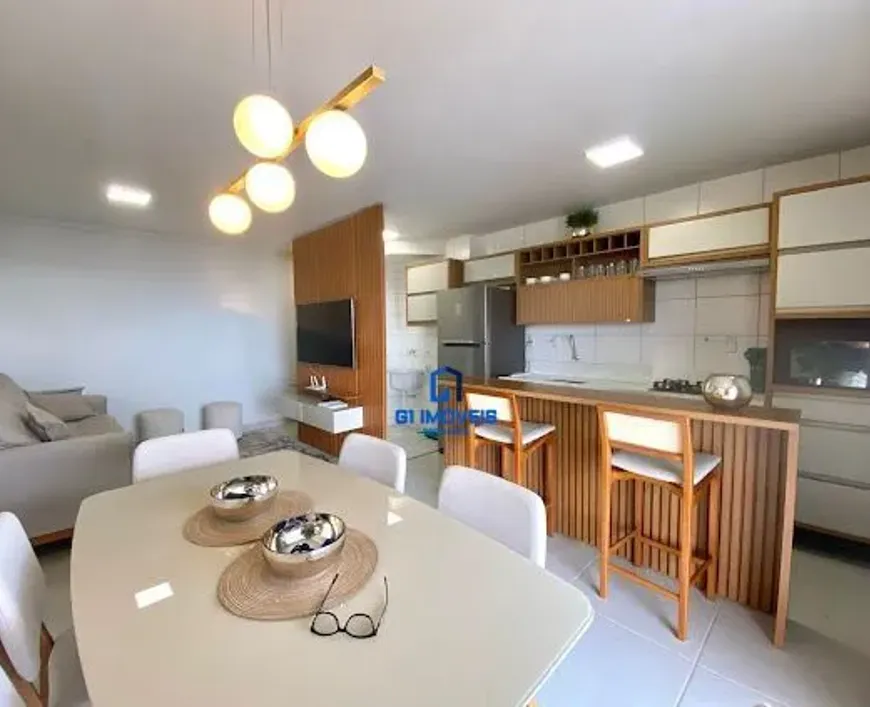 Área de Jantar: Mesa: A mesa retangular possui um tampo em um tom de creme ou bege claro, com um acabamento brilhante que reflete a luz, dando uma sensação de amplitude. As bordas da mesa são levemente arredondadas, adicionando um toque de suavidade ao design. Cadeiras: As cadeiras são brancas, com um design minimalista e elegante. O encosto das cadeiras parece ser ligeiramente curvado para maior conforto, e as pernas são finas e discretas. Sousplats: Os sousplats redondos são feitos de fibra natural, como palha ou vime, com uma textura trançada que adiciona um toque rústico e natural à mesa. Tigelas Decorativas: As tigelas prateadas têm um design moderno e elegante, com uma forma arredondada e um acabamento brilhante que reflete a luz. Elas servem como peças decorativas centrais, adicionando um toque de sofisticação à mesa. Óculos: Os óculos de armação preta adicionam um toque pessoal e casual à mesa, sugerindo que o espaço é usado e habitado. Sala de Estar: Sofá: O sofá bege é espaçoso e convidativo, com almofadas macias e confortáveis que convidam ao relaxamento. O tecido do sofá parece ser macio e texturizado, adicionando um toque de aconchego ao espaço. Pufes: Os pufes redondos são em um tom de cinza claro ou bege, complementando o sofá e oferecendo assentos adicionais. Eles parecem ser feitos de um material macio e confortável, como veludo ou lã. Parede com Painéis de Madeira: A parede com painéis de madeira serve como divisória parcial entre a sala de estar e a cozinha, criando uma sensação de separação sem bloquear completamente a luz e a vista. Os painéis são verticais, adicionando altura e textura à parede. Televisão: A televisão de tela plana está montada na parede, otimizando o espaço e oferecendo uma experiência de visualização imersiva. Móvel Flutuante: O móvel branco flutuante abaixo da TV oferece espaço para armazenamento e exibição de objetos decorativos. Ele parece ser feito de um material liso e brilhante, como MDF laqueado. Cozinha: Armários: Os armários brancos e detalhes em madeira criam um visual limpo e moderno. Os armários superiores são brancos, enquanto os armários inferiores e as prateleiras abertas são de madeira, adicionando calor e textura ao espaço. Bancada: A bancada de madeira clara se estende para formar uma península, criando um espaço informal para refeições ou para sentar enquanto se cozinha. A bancada parece ser feita de uma madeira maciça ou folheada, com um acabamento natural que destaca os grãos da madeira. Banquetas: As banquetas de madeira com assentos brancos estão posicionadas junto à península, criando um espaço informal para refeições ou para sentar enquanto se cozinha. As banquetas têm um design simples e elegante, com pernas finas e um assento confortável. Eletrodomésticos: Os eletrodomésticos modernos de aço inoxidável, como uma geladeira e um micro-ondas, estão integrados ao design da cozinha, adicionando um toque de sofisticação e funcionalidade. Iluminação: Luminária Pendente: A luminária pendente moderna acima da mesa de jantar é uma peça de destaque no espaço. Ela apresenta globos de luz branca presos a uma estrutura de madeira, criando um visual elegante e contemporâneo. Spots de Luz: Spots de luz embutidos no teto garantem uma iluminação uniforme em todo o ambiente, criando uma atmosfera acolhedora e convidativa. Piso: O piso é revestido com azulejos claros, que refletem a luz e ampliam a sensação de espaço. Os azulejos parecem ser grandes e retangulares, com um acabamento liso e brilhante.