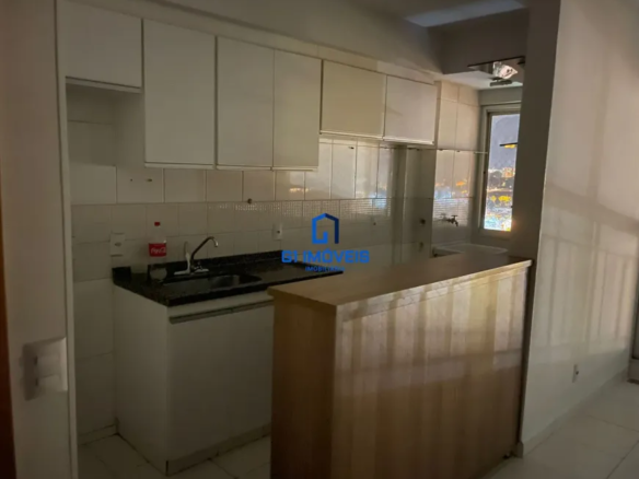 Visão Geral: A imagem captura uma cozinha compacta e funcional, projetada em um estilo moderno e prático. A iluminação é suave e difusa, criando uma atmosfera convidativa e aconchegante. A composição da imagem foca principalmente na área da pia e do balcão, oferecendo uma visão detalhada dos materiais e acessórios utilizados. Detalhes da Parede e Azulejos: As paredes são revestidas com azulejos quadrados de cor creme claro, quase branco. As juntas entre os azulejos são finas e claras, proporcionando uma aparência limpa e uniforme. Há algumas pequenas imperfeições e marcas sutis nos azulejos, sugerindo que a cozinha é utilizada e bem cuidada. Armários Superiores: Os armários superiores são brancos e possuem um acabamento liso e brilhante. As portas são retangulares e sem detalhes ornamentais, com puxadores discretos em metal prateado. A parte superior dos armários acompanha a linha do teto, otimizando o espaço de armazenamento vertical. Bancada e Pia: A bancada é feita de granito preto com pequenos pontos de brilho, conferindo um toque de sofisticação. A pia é de aço inoxidável e possui um design retangular, com cantos arredondados. A torneira é moderna, com um corpo cromado e um design ergonômico. Ao lado da pia, uma garrafa de Coca-Cola vermelha adiciona uma pitada de cor e um toque casual ao ambiente. Balcão de Madeira: O balcão de madeira serve como uma barreira visual e funcional entre a cozinha e outro espaço adjacente. A madeira possui um tom claro e natural, com um acabamento que realça os veios e a textura da madeira. A estrutura do balcão é simples, com painéis verticais que se estendem do chão até a altura da bancada. Iluminação e Vista: A iluminação na cozinha é suave e indireta, criando uma atmosfera agradável. A luz natural entra pela janela, que oferece uma vista noturna da cidade. As luzes da cidade criam um cenário cintilante e colorido, que contrasta com a sobriedade da cozinha. Detalhes Adicionais: Na parede, perto da pia, há uma tomada elétrica com um espelho branco. O piso da cozinha é revestido com cerâmica clara, que complementa a paleta de cores do ambiente. Há uma pequena abertura entre o balcão e a parede, revelando parte do espaço adjacente. A imagem é bem iluminada e possui uma boa profundidade de campo, permitindo que os detalhes sejam vistos com clareza. Em resumo, a cozinha é um espaço funcional e bem projetado, com uma estética moderna e convidativa. A combinação de cores claras, materiais de qualidade e iluminação suave cria um ambiente agradável e acolhedor.