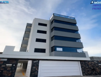 Fachada de prédio moderno no bairro Santa Mônica, Uberlândia (MG), com design minimalista em branco e cinza, varandas de vidro e muro de pedra na entrada.