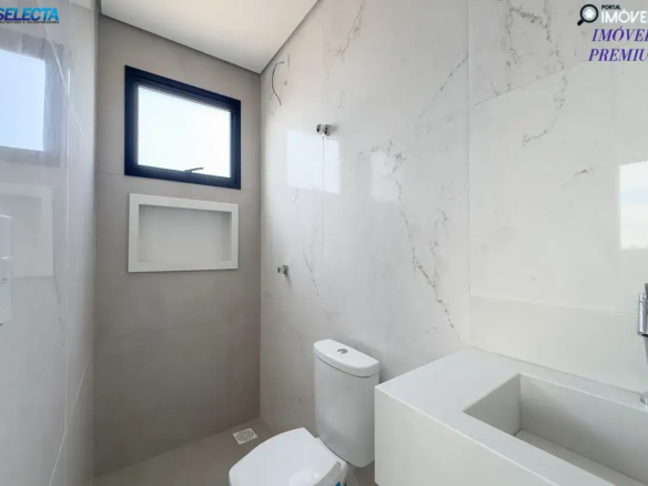 A imagem apresenta o banheiro de um apartamento à venda no bairro Santa Mônica, em Uberlândia, MG, destacando um ambiente moderno e sofisticado. O banheiro exibe um design contemporâneo, com predominância de cores neutras como branco e cinza, que conferem um visual limpo e elegante. A arquitetura é caracterizada por linhas retas e acabamentos de alta qualidade, sugerindo um padrão premium. O ambiente do banheiro parece ser espaçoso e bem iluminado, com detalhes que evidenciam cuidado e sofisticação, como piso e revestimentos de alta qualidade, iluminação estratégica e possivelmente acessórios modernos. O estilo do imóvel reflete um alto padrão, com atenção aos detalhes que proporcionam conforto e funcionalidade. A localização no bairro Santa Mônica, conhecido por sua infraestrutura completa e tranquilidade, é um dos pontos fortes do imóvel. A imagem transmite a ideia de um apartamento de luxo, perfeito para quem deseja viver em um ambiente moderno, confortável e bem localizado em uma das áreas mais valorizadas de Uberlândia.