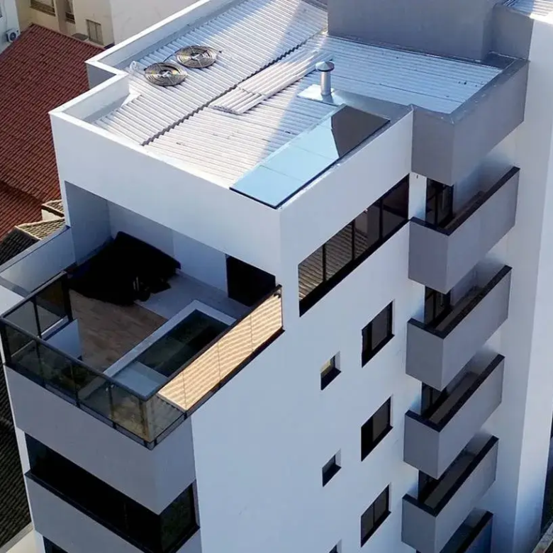 Foco na Fachada e Cobertura do Edifício Meraki, Santa Mônica, Uberlândia: 1. Visão Geral da Imagem: Perspectiva: A imagem nos presenteia com uma visão aérea e angular do Edifício Meraki, permitindo uma análise minuciosa da sua fachada e cobertura. O ângulo escolhido enfatiza a verticalidade do edifício e a relação entre seus elementos arquitetônicos. Enquadramento: O enquadramento da imagem concentra-se na parte superior do edifício, proporcionando uma visão clara e detalhada da sua estrutura, materiais e acabamentos. 2. Fachada: Uma Expressão de Modernidade e Elegância: Design: A fachada do Edifício Meraki expressa um design moderno e minimalista, com linhas retas e volumes geométricos bem definidos. A ausência de elementos decorativos excessivos enfatiza a pureza das formas e a elegância do conjunto. Cores: A paleta de cores da fachada é composta por tons neutros e suaves, como branco e cinza. O branco confere luminosidade e amplitude ao edifício, enquanto o cinza adiciona um toque de sofisticação e sobriedade. As janelas escuras criam um contraste marcante com os painéis claros, acentuando a verticalidade da construção. Sacadas: As sacadas do Edifício Meraki são integradas à fachada, com um design discreto e elegante. Os guarda-corpos de vidro proporcionam segurança e privacidade aos moradores, sem comprometer a vista da cidade. As sacadas criam uma sensação de continuidade entre o interior e o exterior dos apartamentos, ampliando os espaços e permitindo o contato com a natureza. Janelas: As janelas retangulares da fachada são amplas e generosas, permitindo a entrada abundante de luz natural nos apartamentos. As molduras escuras das janelas criam um contraste elegante com os painéis claros da fachada, acentuando a verticalidade do edifício. Painéis: A fachada do Edifício Meraki é composta por painéis pré-fabricados, que garantem a qualidade, a durabilidade e a rapidez da construção. Os painéis apresentam um acabamento liso e uniforme, conferindo um aspecto moderno e sofisticado ao edifício. 3. Cobertura: Um Espaço de Lazer e Bem-Estar: Design: A cobertura do Edifício Meraki apresenta um design inovador e funcional, com diferentes níveis e espaços de convivência. A área de lazer na cobertura é um oásis de bem-estar e entretenimento, com piscina, solarium, churrasqueira e outros ambientes projetados para o conforto e a diversão dos moradores. Materiais: A cobertura do Edifício Meraki é revestida com materiais de alta qualidade e resistência, como telhas metálicas, mantas impermeabilizantes e porcelanatos antiderrapantes. Os materiais escolhidos garantem a durabilidade, a segurança e a beleza do espaço. Piscina: A piscina na cobertura é um dos destaques do Edifício Meraki, oferecendo um espaço para relaxamento, prática de esportes e convívio social. A água cristalina da piscina reflete o céu e a paisagem urbana, criando uma atmosfera mágica e inspiradora. Telhado: A cobertura telhado do edifício é telhado com telhas metálicas, com um bom sistema de escoamento de aguas pluvias. Equipamentos: A cobertura do Edifício Meraki abriga diversos equipamentos técnicos, como aparelhos de ar condicionado, caixas d'água e chaminés. Os equipamentos são instalados de forma organizada e discreta, sem comprometer a estética do espaço. Vista: A cobertura do Edifício Meraki oferece uma vista privilegiada da cidade de Uberlândia. Os moradores podem desfrutar de paisagens panorâmicas, pores do sol inesquecíveis e momentos de lazer em um ambiente exclusivo e sofisticado. 4. Relação com o Entorno: Integração: A arquitetura do Edifício Meraki busca integrar-se harmoniosamente com o entorno urbano de Santa Mônica. O edifício respeita a escala do bairro, com uma altura que não compromete a vista dos vizinhos e um design que não destoa das construções existentes. Valorização: A construção do Edifício Meraki contribui para a valorização do bairro Santa Mônica, atraindo novos moradores e investidores e impulsionando o desenvolvimento da região. Palavra chave Apartamento à Venda com 3 Quartos 93m² no Setor Santa Mônica