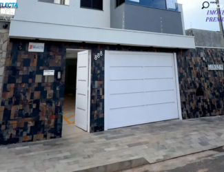 Fachada de imóvel com muro revestido em pedra escura. Destaque para o portão e a porta de entrada brancos, a inscrição 
