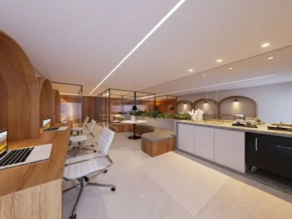 Visão Geral do Ambiente: A imagem retrata um espaço de trabalho ou convivência moderno e bem iluminado, provavelmente um coworking, lounge de escritório ou área comum de um edifício residencial/comercial. A atmosfera é sofisticada e funcional, combinando elementos de design contemporâneo com materiais quentes. Detalhes do Imóvel: Layout e Estrutura: O espaço é amplo e parece dividido em zonas funcionais distintas. À esquerda, há uma área de trabalho individualizada; no centro, uma zona de estar mais informal; e à direita, uma copa ou área de café. Ao fundo, percebe-se uma área separada por divisórias de vidro. Cores Predominantes: A paleta de cores é majoritariamente neutra e clara, contribuindo para a sensação de amplitude e luminosidade. Predominam o branco (teto, paredes, cadeiras, parte dos armários), tons de bege/creme (piso, bancada), cinza (estofado do banco, tampo da bancada) e o tom quente da madeira clara/média (arcos, mesas, base do banco, painéis). O preto surge em detalhes pontuais (bases das mesas, luminárias pendentes, molduras das divisórias de vidro, eletrodoméstico). O verde das plantas adiciona um toque de cor natural. Mobiliário e Acabamentos: Área de Trabalho (Esquerda): O destaque são as grandes estruturas em arco feitas de madeira clara, que criam estações de trabalho semi-privativas. Cada nicho possui uma bancada de trabalho do mesmo material, equipada com um laptop. As cadeiras são de escritório, modelo "Eames" ou similar, com assento e encosto brancos (provavelmente couro sintético ou plástico) e base cromada giratória com rodízios. Área de Estar (Centro): Um banco curvo embutido acompanha a parede, com base revestida em madeira e assento estofado em tecido cinza. À frente dele, uma pequena mesa redonda com tampo branco e base preta. Atrás do banco, um canteiro elevado com plantas verdes. Copa/Balcão (Direita): Uma longa bancada com tampo que parece ser de pedra (granito ou quartzo) em tons de cinza/bege salpicado. Os armários inferiores são predominantemente brancos, com puxadores discretos ou inexistentes (sistema de clique). Há um eletrodoméstico preto embutido (possivelmente um frigobar ou adega pequena). Sobre a bancada, há itens típicos de uma copa: suportes com copos, bandejas, talvez uma máquina de café (parcialmente visível). Fundo: Divisórias de vidro com esquadrias pretas separam outra área, onde se pode ver mais painéis de madeira e possivelmente mais mesas. Iluminação: O teto é branco e liso. A iluminação é um ponto forte do design: Uma longa linha de luz LED embutida atravessa o teto diagonalmente, oferecendo iluminação geral e um elemento de design marcante. Spots de luz embutidos (downlights) estão distribuídos pelo teto, principalmente sobre a área da copa. Luminárias pendentes com cúpulas pretas são usadas como iluminação de destaque sobre a mesa redonda central e dentro dos nichos decorativos na parede atrás da copa. Piso: O piso é revestido com peças grandes de porcelanato ou material similar, em tom bege claro ou off-white, de acabamento fosco ou acetinado. Paredes e Detalhes Arquitetônicos: As paredes são predominantemente brancas. Um detalhe interessante é a repetição do motivo de arco: os grandes arcos de madeira das estações de trabalho são ecoados por nichos em arco menores na parede atrás da copa, cada um com uma luminária pendente, criando ritmo e coesão visual. Ambiência Geral: O ambiente transmite uma sensação de profissionalismo e conforto. É um espaço projetado para ser ao mesmo tempo funcional para o trabalho e agradável para pausas ou interações sociais. O uso da madeira e das plantas aquece o design moderno e predominantemente neutro, tornando-o acolhedor. A iluminação bem planejada contribui para um espaço claro e convidativo.