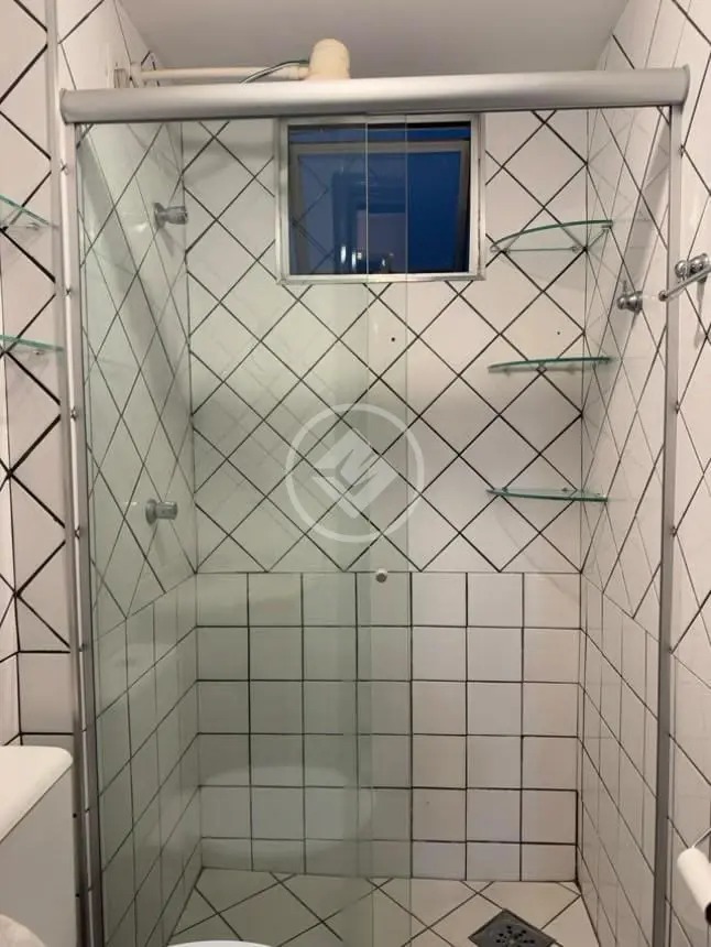 Detalhe do box de vidro do banheiro com revestimento cerâmico branco e prateleiras de vidro no Residencial Hayward.