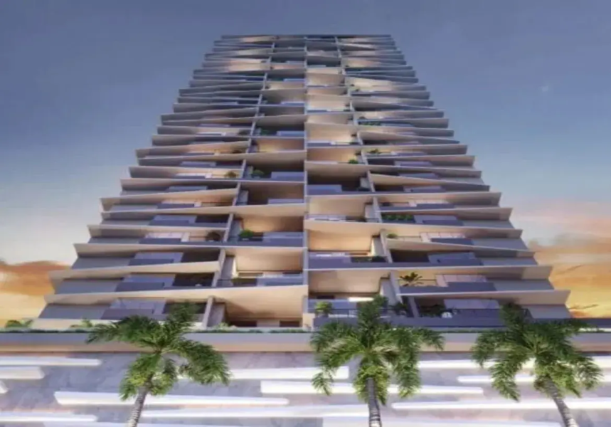 A imagem apresenta um edifício residencial de múltiplos andares, muito alto e com arquitetura moderna e arrojada. A perspectiva é de baixo para cima (contra-plongée), o que enfatiza a imponência e a altura da construção. Detalhes do Imóvel: Estrutura e Design: O prédio possui um design único e dinâmico, caracterizado por suas lajes e varandas que não seguem um alinhamento vertical reto. Cada andar parece ter suas varandas projetadas para fora em ângulos ligeiramente diferentes, criando um efeito visual escalonado, facetado ou quase "torcido" à medida que o prédio sobe. Isso confere movimento e originalidade à fachada. As varandas são amplas. Cores: A paleta de cores é predominantemente neutra e sofisticada. A estrutura principal do edifício (lajes, pilares visíveis) é de um tom claro, possivelmente concreto aparente, bege ou cinza muito claro. As áreas recuadas das varandas e as esquadrias das grandes janelas/portas de vidro são mais escuras, em tons de cinza chumbo ou azul-acinzentado. O vidro das janelas reflete o céu, variando entre tons escuros e reflexos mais claros. Materiais: Visualmente, percebe-se o uso de concreto (ou material similar de revestimento claro) para as lajes e estrutura, e muito vidro nas fachadas dos apartamentos, provavelmente do chão ao teto para maximizar a vista e a luz natural. A base do prédio parece ter um revestimento diferente, talvez painéis de mármore ou pedra clara, com detalhes horizontais que podem ser elementos de iluminação ou decorativos. Iluminação e Ambiente: A iluminação sugere ser o final da tarde ou início da noite (crepúsculo). O céu ao fundo tem gradientes de cores quentes (laranja/amarelo) perto do horizonte (visível sutilmente à direita) que se fundem com tons mais frios (azul escuro/roxo) no topo. Algumas luzes estão acesas dentro dos apartamentos e nas áreas comuns das varandas, emitindo um brilho quente (amarelado/branco), que contrasta com a luz ambiente mais fria do céu. Isso cria uma atmosfera elegante e acolhedora. Móveis e Paisagismo: Devido à distância e ao ângulo, não é possível distinguir móveis específicos nas varandas. No entanto, em algumas delas, percebem-se volumes que sugerem a presença de plantas (pequenas árvores ou arbustos em vasos), adicionando um toque de verde. Na base do prédio, em primeiro plano, há várias palmeiras altas e esguias, com folhagem verde vibrante, que contribuem para a ambientação e dão um toque tropical ou de resort de luxo. Resumo: A imagem retrata um arranha-céu residencial de luxo com um design arquitetônico inovador e marcante, caracterizado por suas varandas anguladas e desalinhadas. As cores neutras, a iluminação crepuscular e a presença de vegetação criam uma atmosfera sofisticada e moderna.