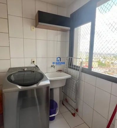 Lavanderia funcional com máquina de lavar inox, tanque e janela com rede de proteção.