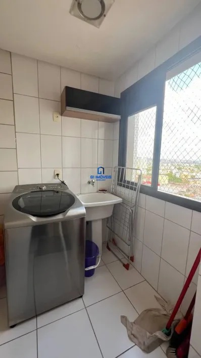 Lavanderia funcional com máquina de lavar inox, tanque e janela com rede de proteção.