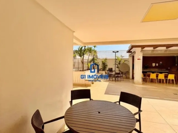 Área gourmet externa coberta com churrasqueira, mesas redondas e cadeiras de vime para eventos sociais.