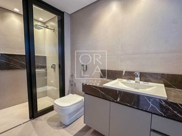 Banheiro suíte com revestimento cinza e iluminação focal no espelho.