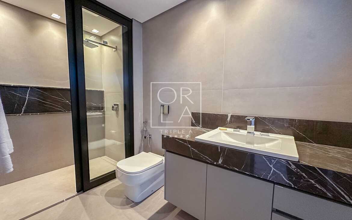 Banheiro suíte com revestimento cinza e iluminação focal no espelho.