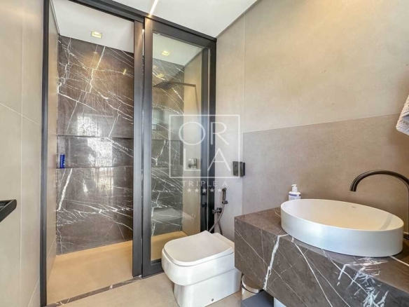 Box de banheiro com revestimento escuro, chuveiro de teto e bancada em pedra.