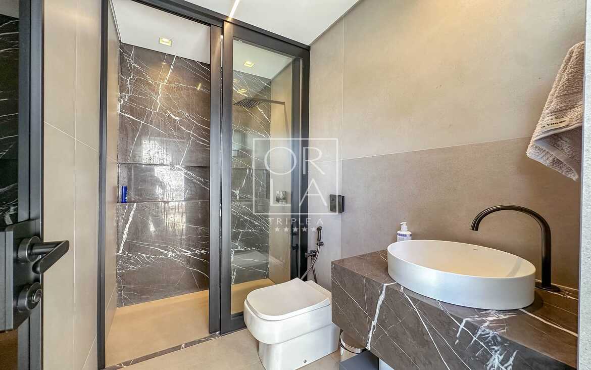 Box de banheiro com revestimento escuro, chuveiro de teto e bancada em pedra.