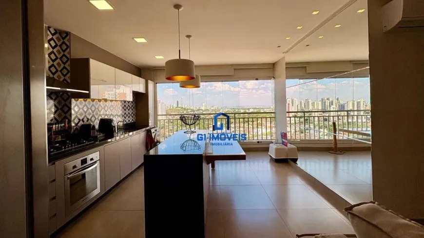 Cozinha com ilha central em granito preto e vista panorâmica para a cidade através da sacada de vidro no Residencial Auge.