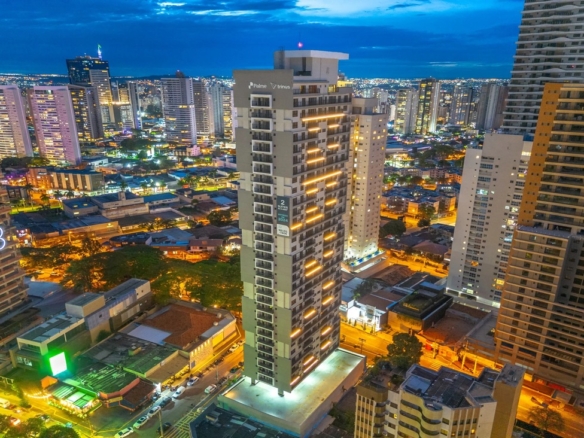 Vista externa noturna do edifício Tempus, destacando a iluminação linear da fachada e a altura do prédio na cidade.