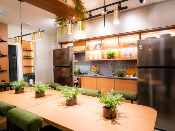 Mesa de jantar integrada à cozinha com cadeiras verdes, geladeira em inox e iluminação pendente moderna.