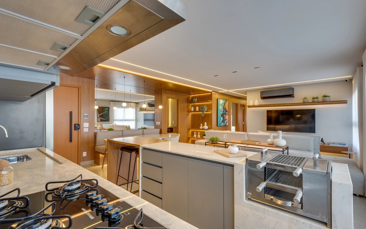 Detalhe de cozinha gourmet com bancada de mármore, cooktop e churrasqueira integrada com acabamento em aço inox.