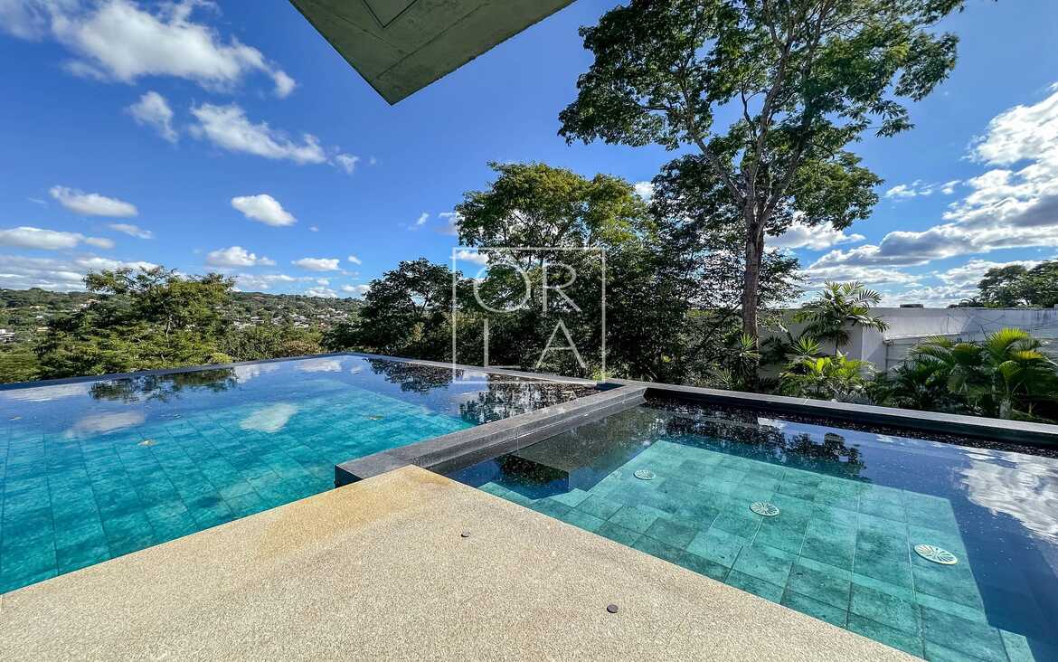 Piscina de borda infinita com revestimento em tons de verde e deck seco.
