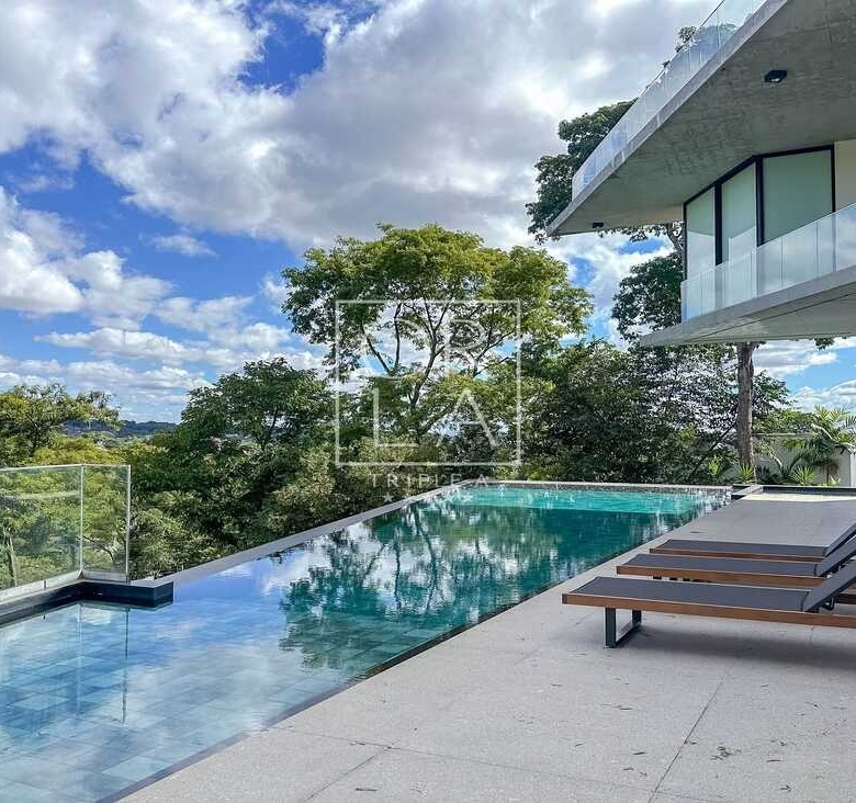Piscina de borda infinita com vista para área verde e espreguiçadeiras.