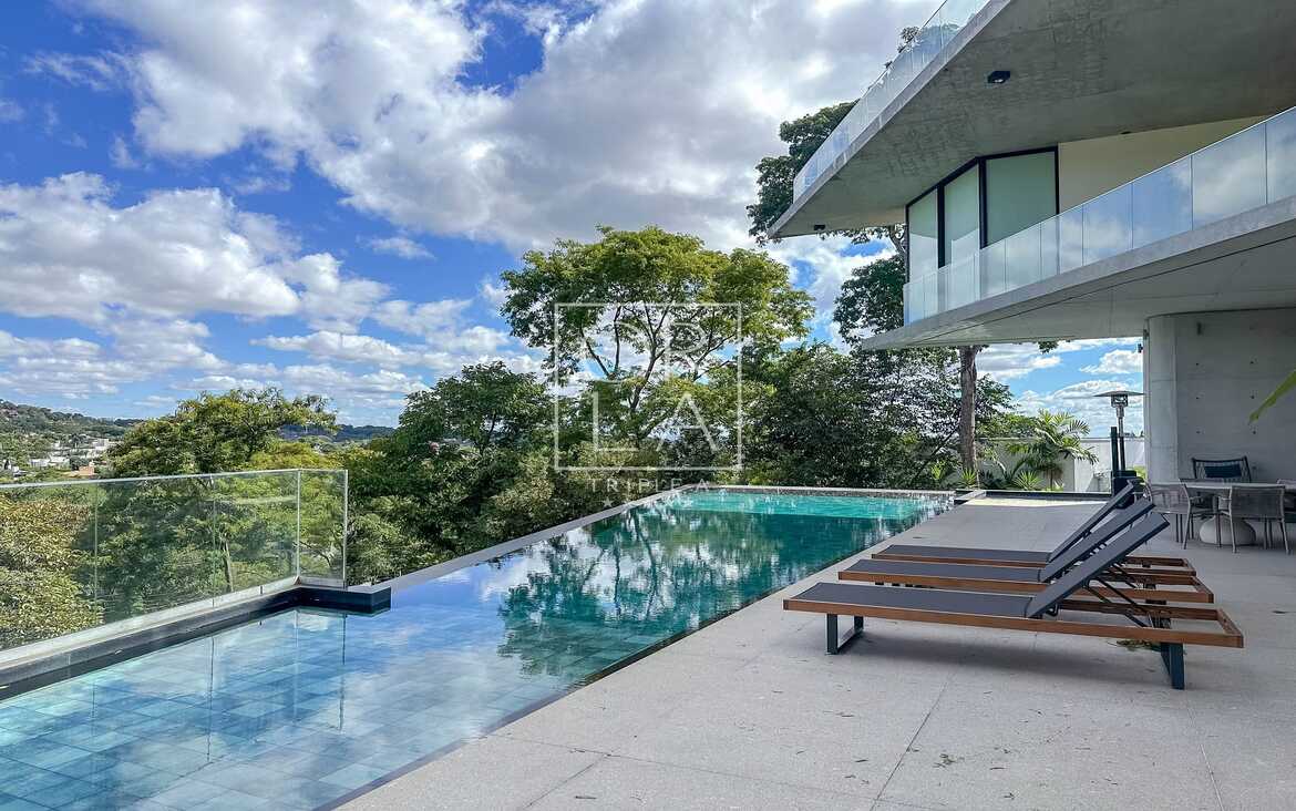 Piscina de borda infinita com vista para área verde e espreguiçadeiras.