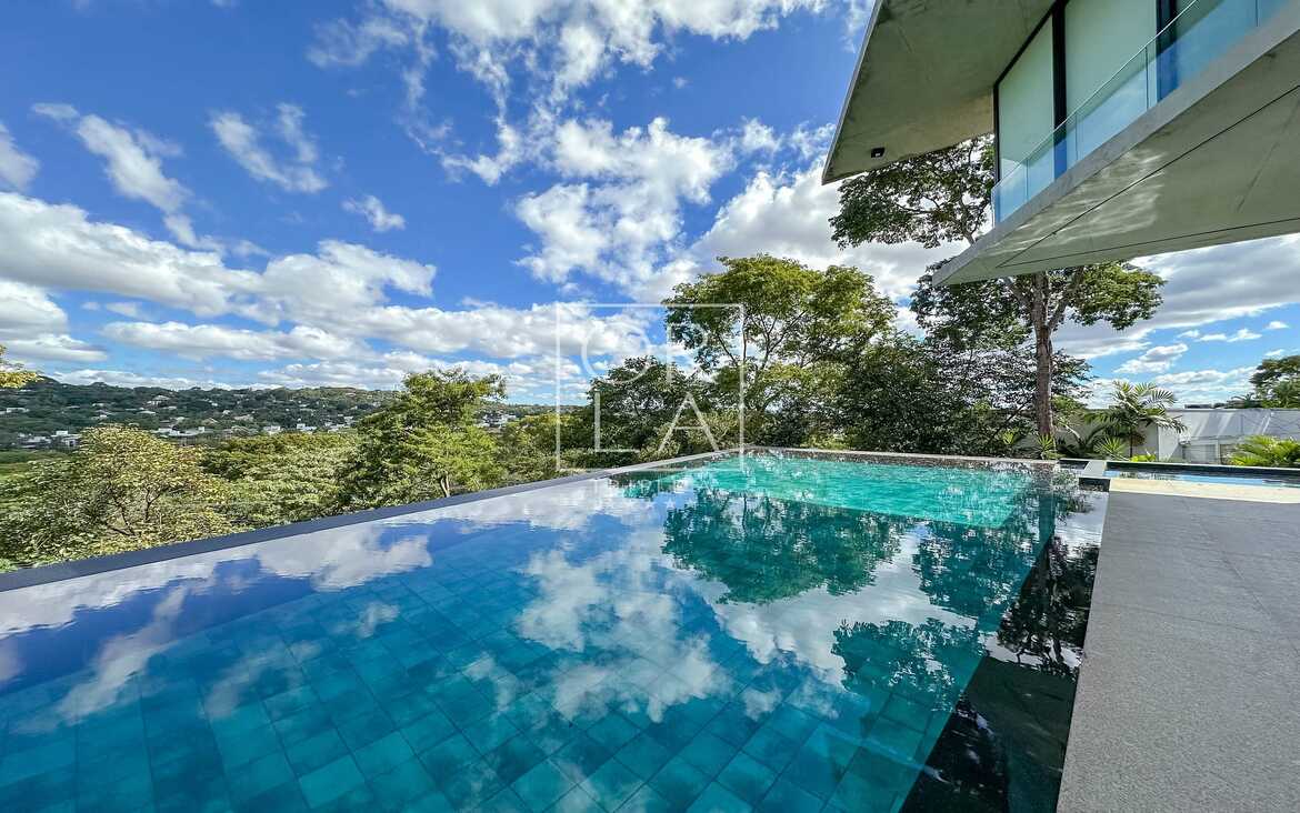Piscina privativa com reflexo do céu e vegetação densa no Aldeia do Vale.