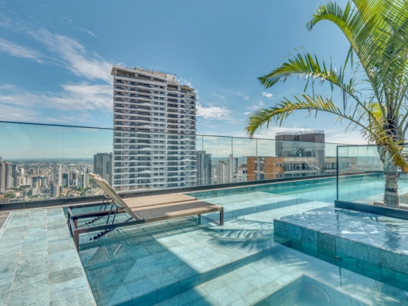 Piscina com deck de azulejos azuis no terraço, espreguiçadeiras e vista para outros arranha-céus sob céu azul.