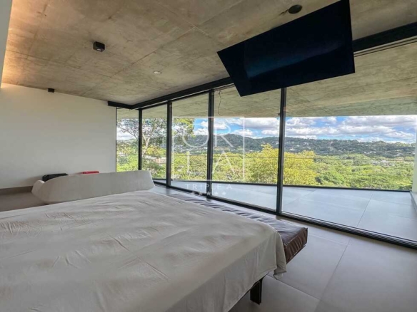 Quarto moderno com televisão embutida no teto e vista para o verde.