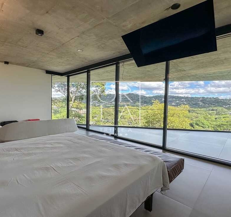 Quarto moderno com televisão embutida no teto e vista para o verde.