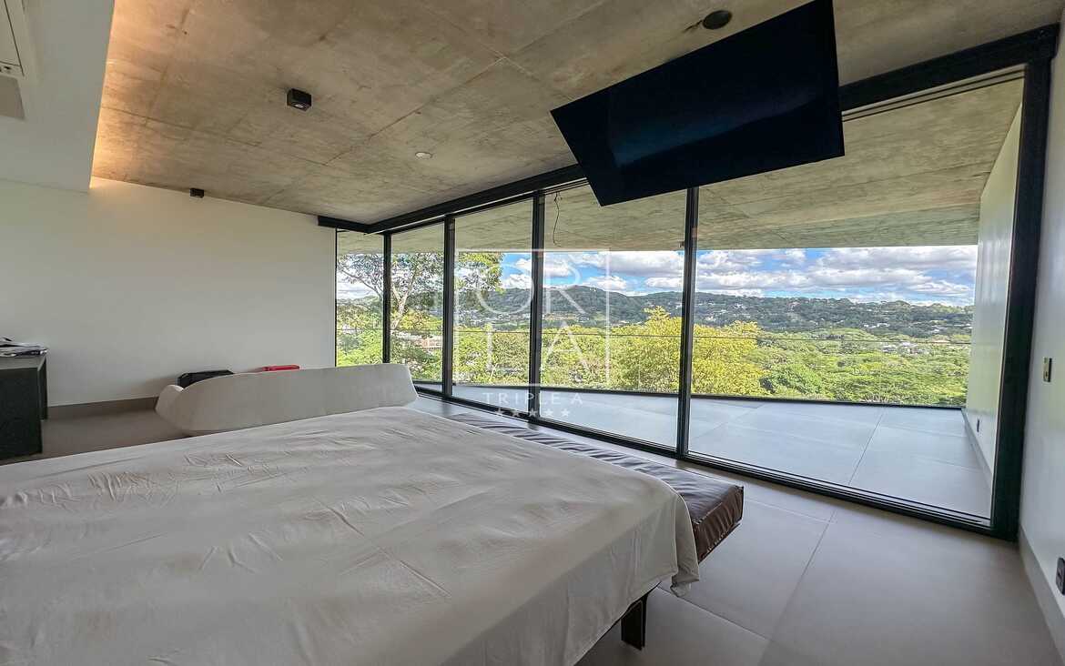 Quarto moderno com televisão embutida no teto e vista para o verde.