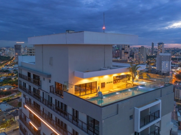 Área de lazer no topo do edifício com piscina iluminada e vista panorâmica da cidade ao entardecer.
