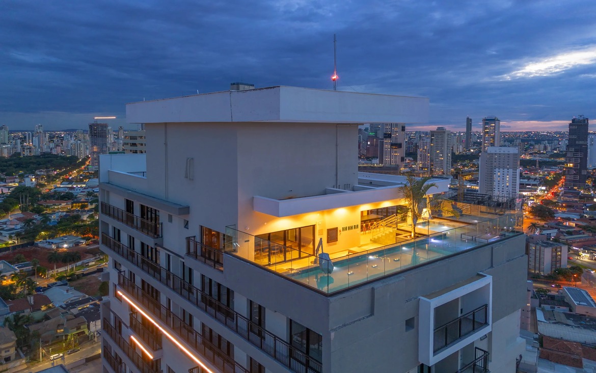 Área de lazer no topo do edifício com piscina iluminada e vista panorâmica da cidade ao entardecer.