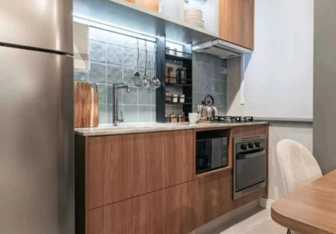 Cozinha planejada com armários de madeira, bancada clara e iluminação em LED em imóvel Now Praça C8 no Setor Sudoeste, Goiânia.