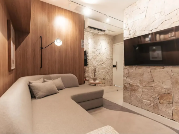 Sala de estar com painel de madeira e parede de pedra no apartamento decorado do Now Praça C8, Setor Sudoeste.