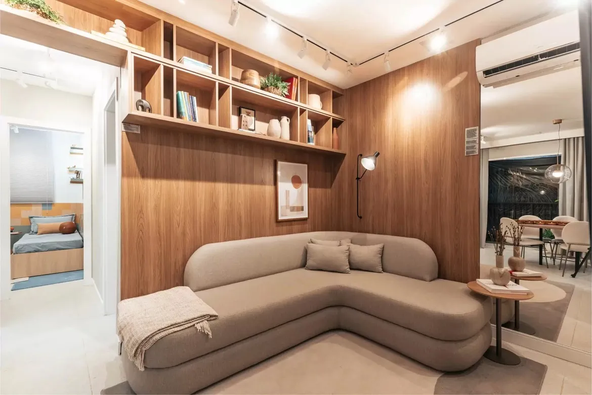 Sala de estar com estante embutida de madeira e sofá de design curvo no apartamento decorado do Now Praça C8, Setor Sudoeste.