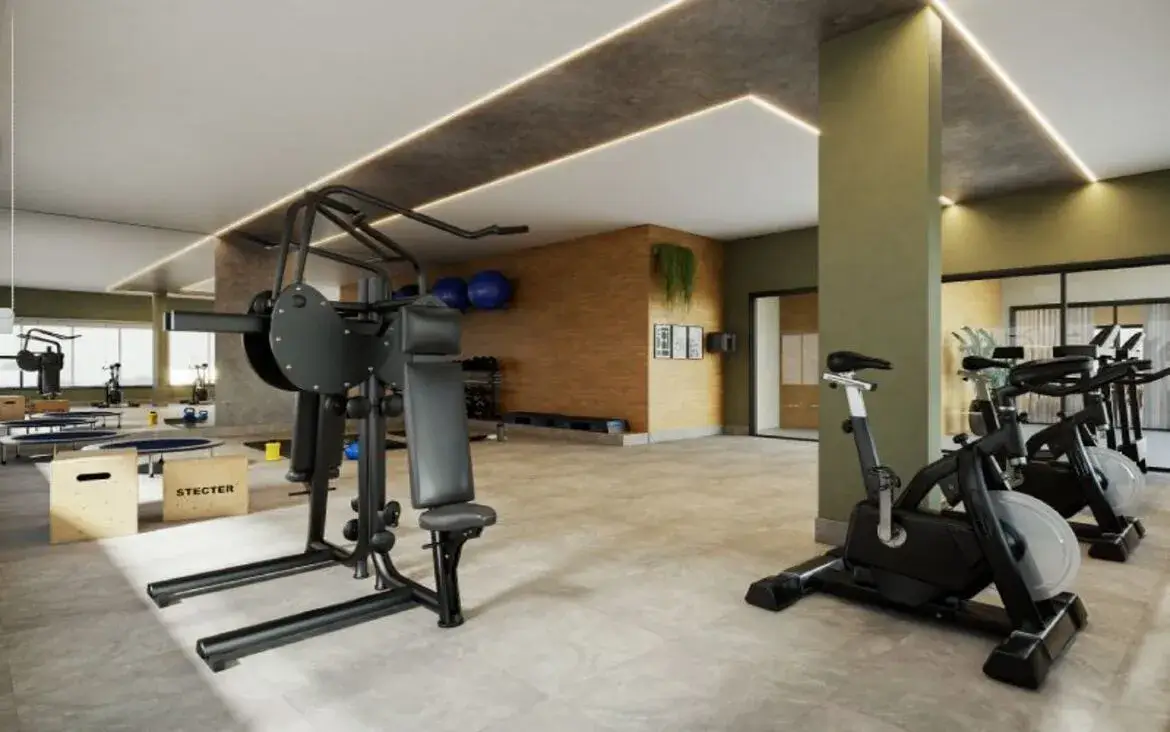 Academia do condomínio bem iluminada, equipada com bicicletas ergométricas e aparelhos de musculação.