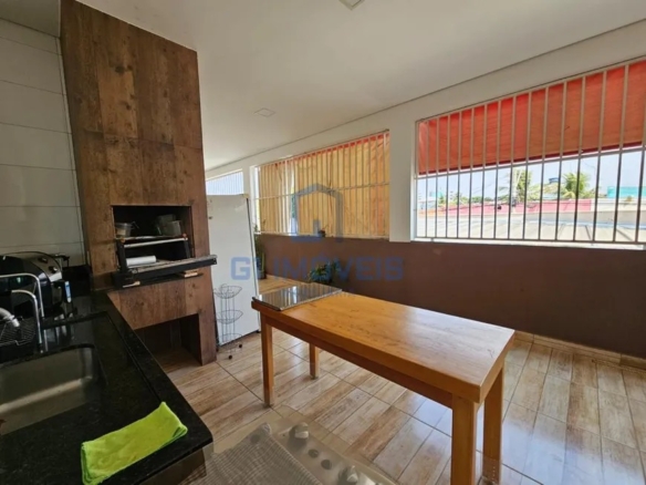 Área gourmet com churrasqueira revestida, pia de granito preto e mesa de madeira rústica.