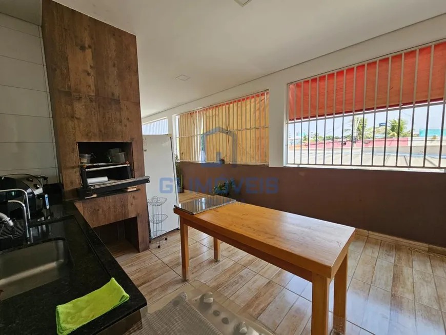 Área gourmet com churrasqueira revestida, pia de granito preto e mesa de madeira rústica.