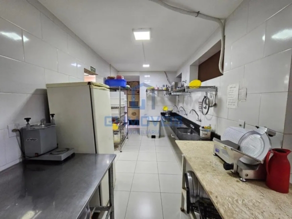 Área de produção da cozinha com freezers verticais, bancadas de inox e revestimento cerâmico.