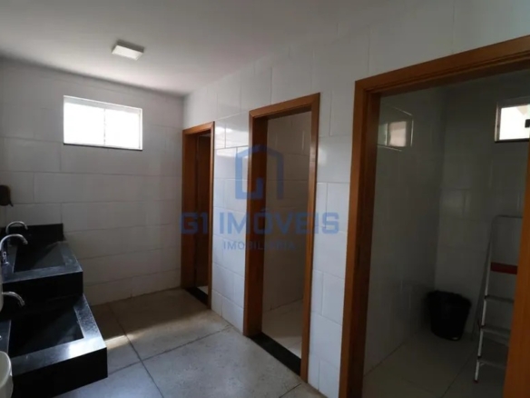 Banheiro coletivo comercial com bancada de granito preto, duas cubas e portas de madeira.