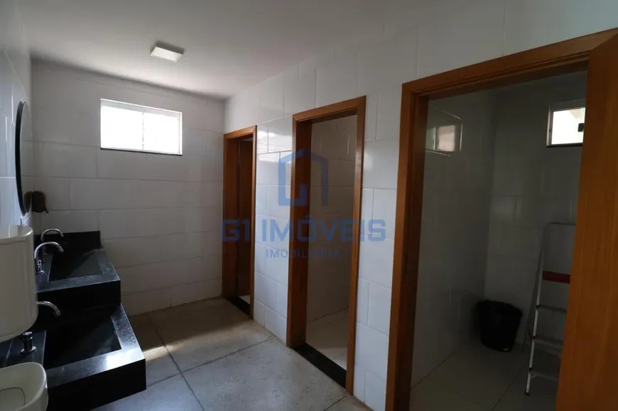 Banheiro coletivo comercial com bancada de granito preto, duas cubas e portas de madeira.