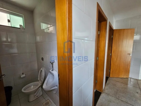 Banheiro masculino comercial com mictório, vaso sanitário e revestimento cerâmico branco.