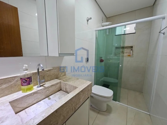 Banheiro social com box de vidro verde, bancada de mármore travertino e armário com espelho.