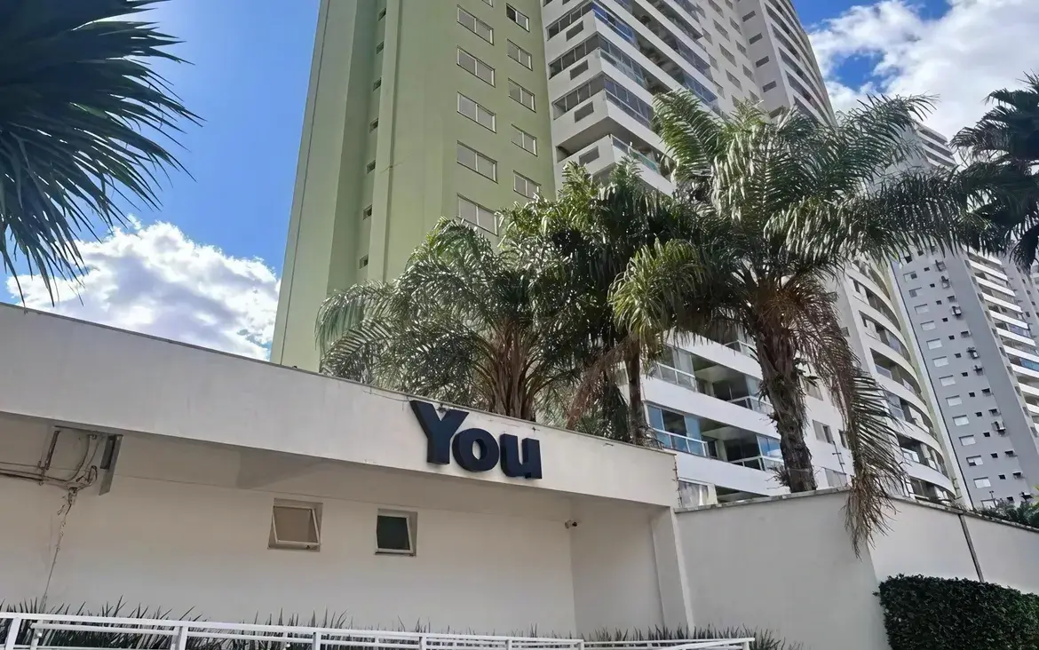 Fachada do prédio com letreiro na entrada e jardim com palmeiras no Condomínio Residencial You.