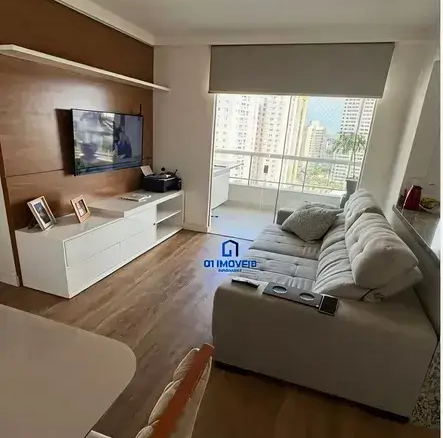 Sala de estar com sofá cinza, rack branco e painel amadeirado no Condomínio Residencial You.